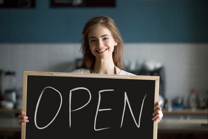 Lächelnde Frauenholding öffnen die Zeichentafel, die zum neuen Café einlädt lizenzfreies stockbild Lächelnde Frauenholding öffnen die Zeichentafel, die zum neuen Café einlädt lizenzfreies stockbild