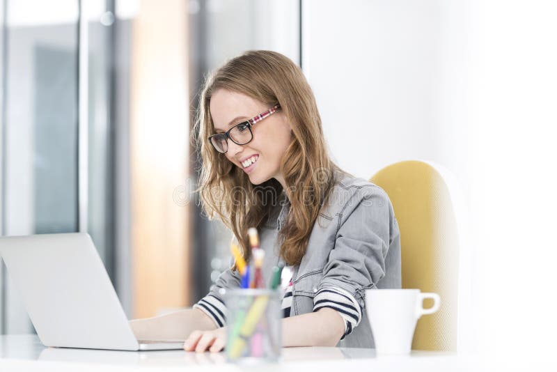 Lächelnde Geschäftsfrau, die eine E-Mail auf Laptop im Büro liest stockfotos Lächelnde Geschäftsfrau, die eine E-Mail auf Laptop im Büro liest stockfotos