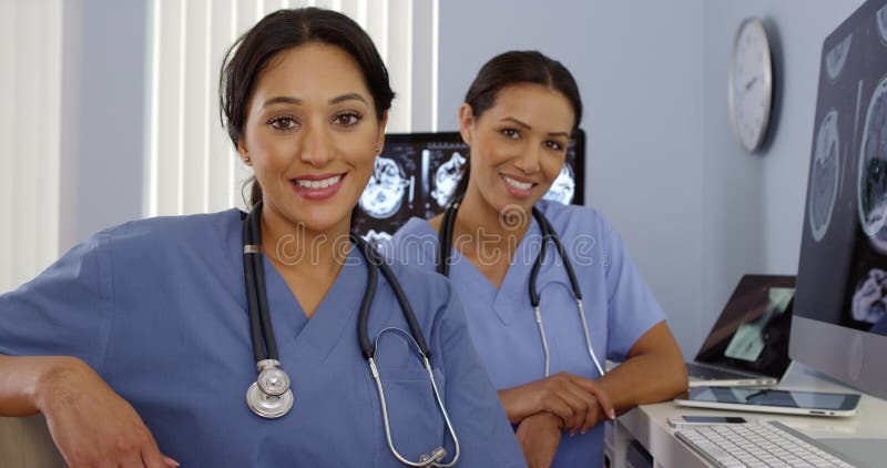 Lächelnde Hispano-Amerikaner- und Afroamerikanerkrankenschwestern, die an der Computerstation sitzen lizenzfreies stockfoto Lächelnde Hispano-Amerikaner- und Afroamerikanerkrankenschwestern, die an der Computerstation sitzen lizenzfreies stockfoto