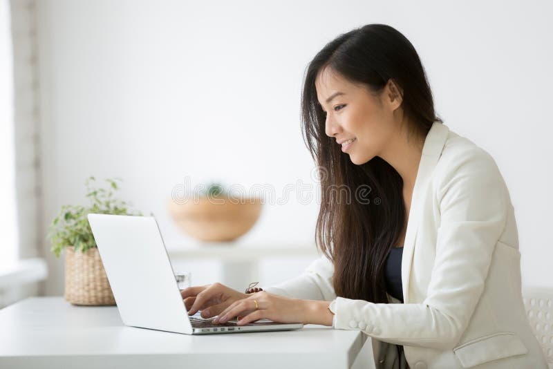 Lächelnde junge asiatische Geschäftsfrau, die den Computer online arbeitet verwendet lizenzfreie stockbilder