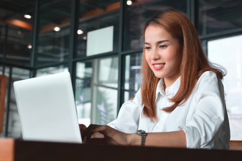 Lächelnde junge asiatische Geschäftsfrau mit Laptopfunktion im modernen Büro lizenzfreie stockbilder Lächelnde junge asiatische Geschäftsfrau mit Laptopfunktion im modernen Büro lizenzfreie stockbilder