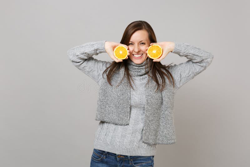 Lächelnde junge Frau in der grauen Strickjacke, Schalgrifforangen lokalisiert auf grauem Wandhintergrund, Studioporträt Gesund lizenzfreie stockfotos Lächelnde junge Frau in der grauen Strickjacke, Schalgrifforangen lokalisiert auf grauem Wandhintergrund, Studioporträt Gesund lizenzfreie stockfotos