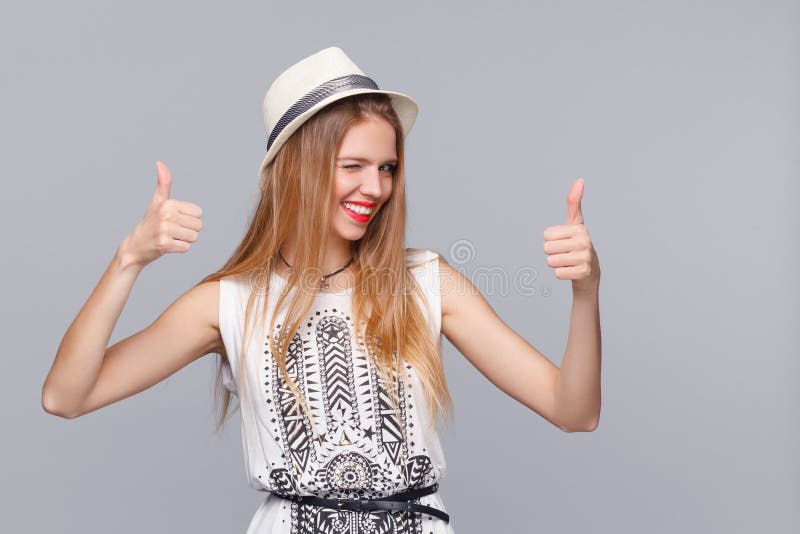Lächelnde junge Frau, die sich Daumen, auf grauem Hintergrund zeigt Glückliches froh blinzelndes Mädchen stockbild Lächelnde junge Frau, die sich Daumen, auf grauem Hintergrund zeigt Glückliches froh blinzelndes Mädchen stockbild