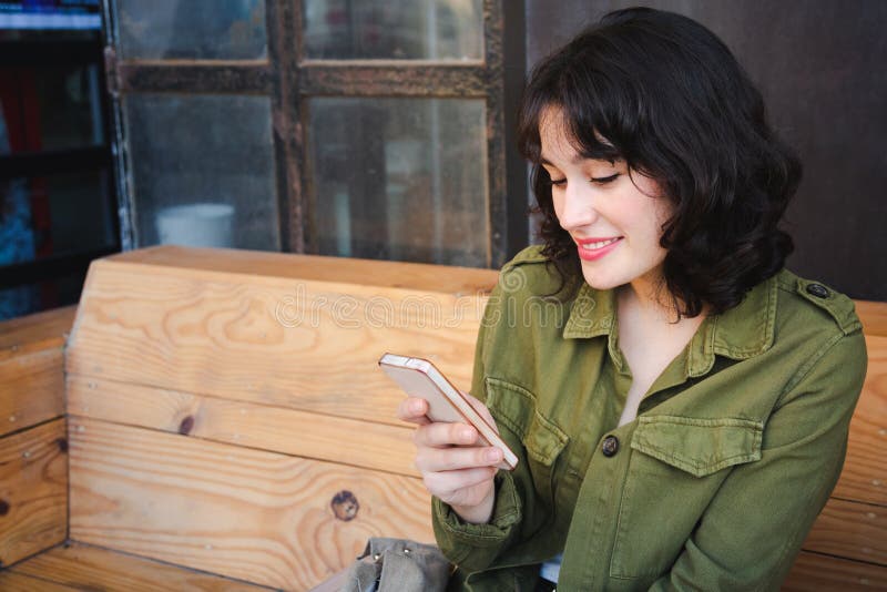 Lächelnde junge Frau unter Verwendung ihres intelligenten Telefons an einer Caféstange lizenzfreie stockfotos Lächelnde junge Frau unter Verwendung ihres intelligenten Telefons an einer Caféstange lizenzfreie stockfotos