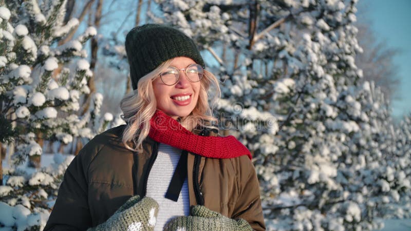 Lächelnde junge schöne Frau entspannt sich und macht Spaß beim Stellen im sonnigen Winterwald mit schneebedeckter Fichte