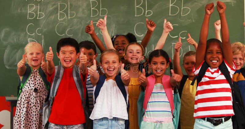 Lächelnde Kinder, die Daumen oben im Klassenzimmer zeigen