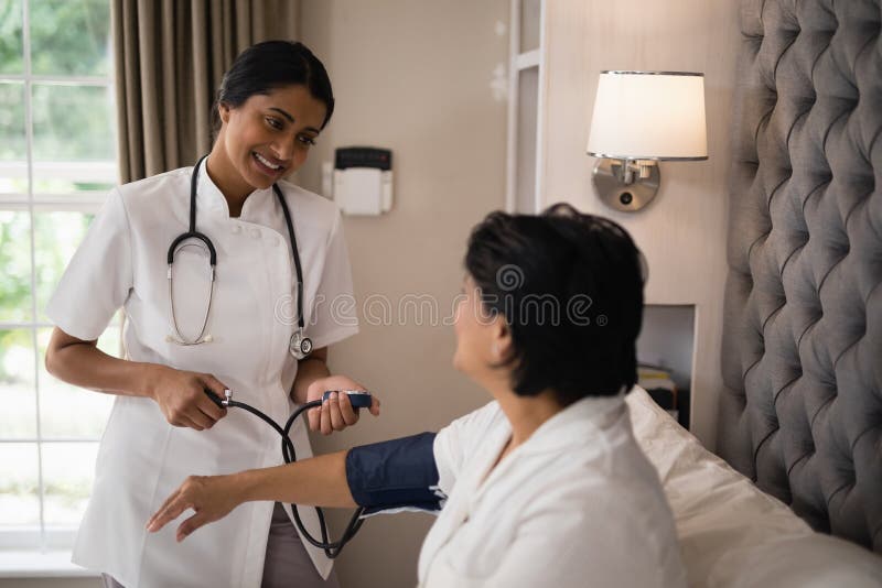 Lächelnde Krankenschwester, die den Blutdruck des Patienten stillstehend auf Bett überprüft lizenzfreies stockbild Lächelnde Krankenschwester, die den Blutdruck des Patienten stillstehend auf Bett überprüft lizenzfreies stockbild