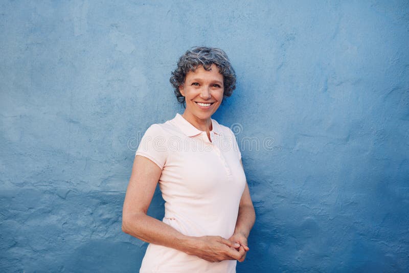 Lächelnde reife Frau, die gegen blauen Hintergrund steht stockfoto Lächelnde reife Frau, die gegen blauen Hintergrund steht stockfoto