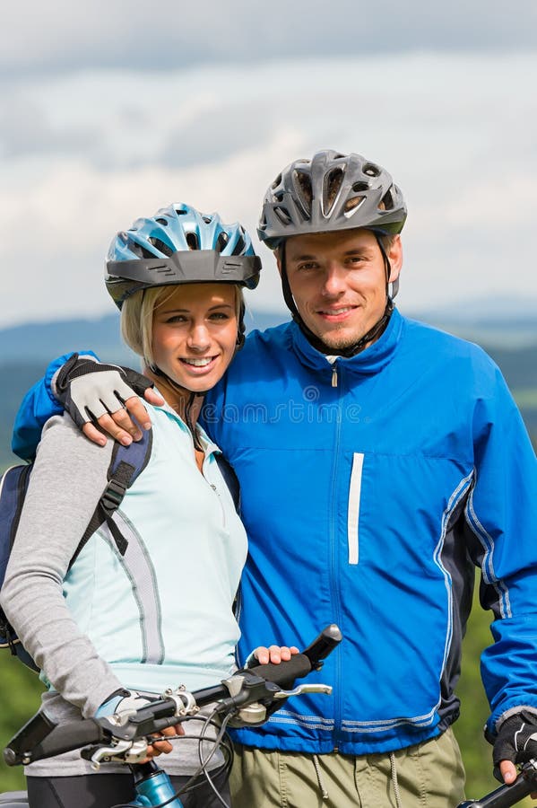Junge sportliche Paare mit Mountainbiken im Sturzhelm lizenzfreie stockbilder Junge sportliche Paare mit Mountainbiken im Sturzhelm lizenzfreie stockbilder
