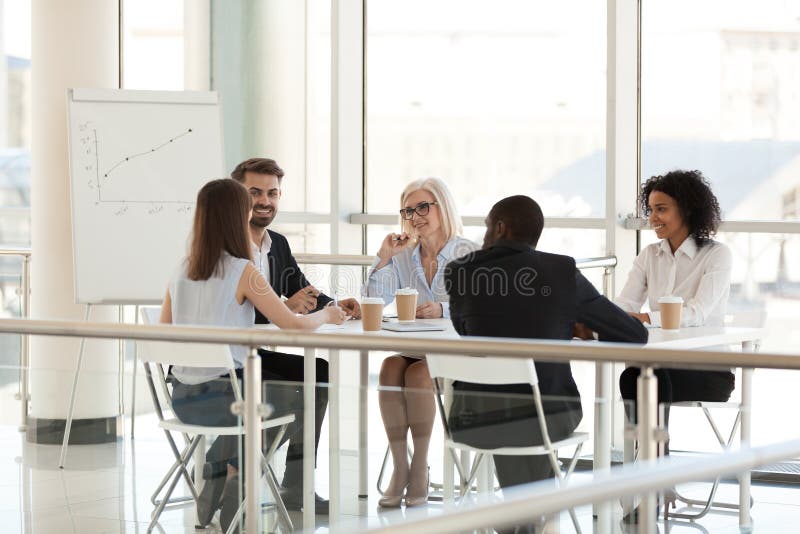 Lächelnde verschiedene Angestellte, die an Versammlungstisch in der Konferenz sprechen stockbild Lächelnde verschiedene Angestellte, die an Versammlungstisch in der Konferenz sprechen stockbild