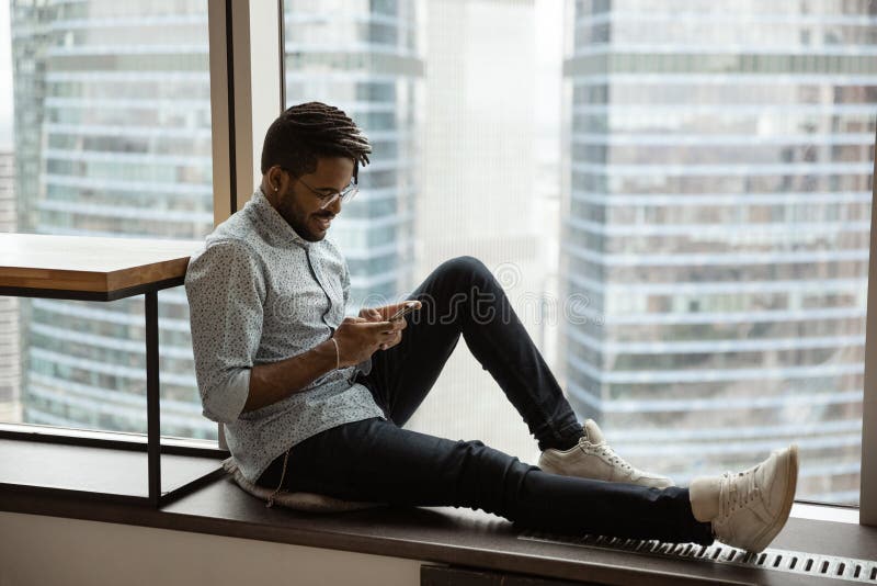 Lächelnder Afroamerikanermann der Datenzugriffsseiten-Ansicht mithilfe des Telefons Nähe Fenster lizenzfreies stockfoto