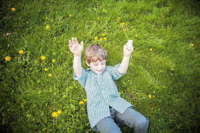 Lächelnder glücklicher Junge, der in Gras außerhalb der Ernte von Blumen legt lizenzfreies stockfoto Lächelnder glücklicher Junge, der in Gras außerhalb der Ernte von Blumen legt lizenzfreies stockfoto