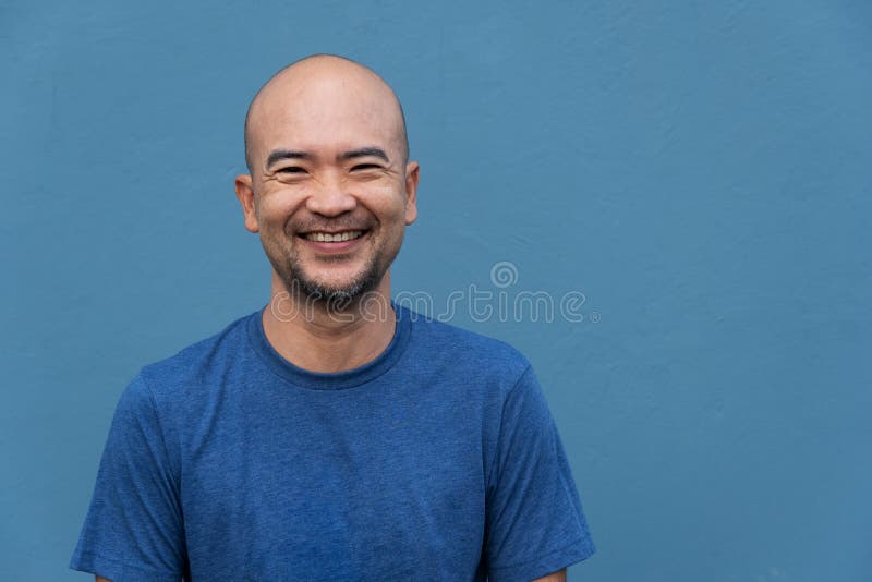 Lächelnder Japanische Porträtmann des düsteren Bartes mit T-Shirt auf Blue Mauer Zement stockfotos