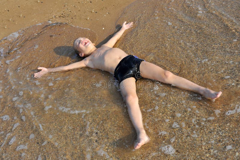 Lächelnder Junge, der im Wasser am Strand liegt stockbild Lächelnder Junge, der im Wasser am Strand liegt stockbild