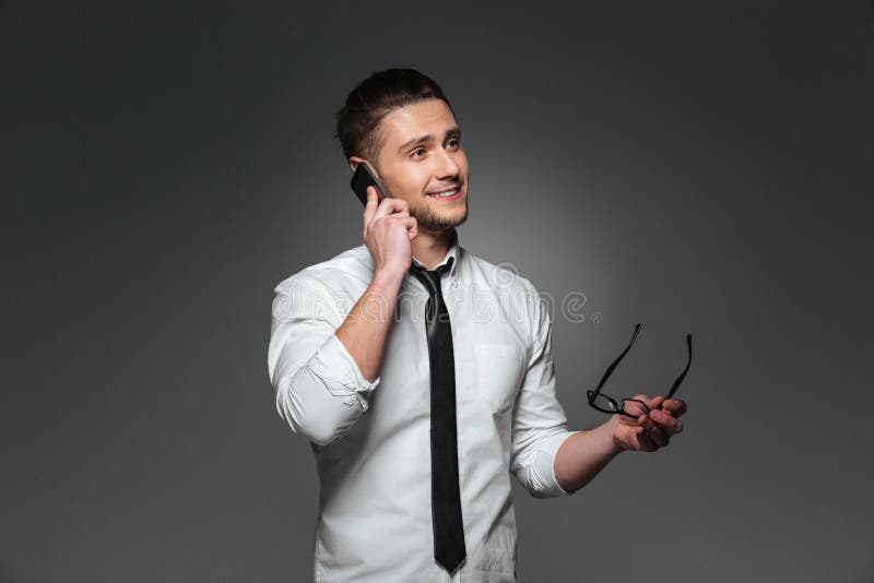 Lächelnder junger Geschäftsmann, der Gläser hält und am Handy spricht lizenzfreies stockbild Lächelnder junger Geschäftsmann, der Gläser hält und am Handy spricht lizenzfreies stockbild