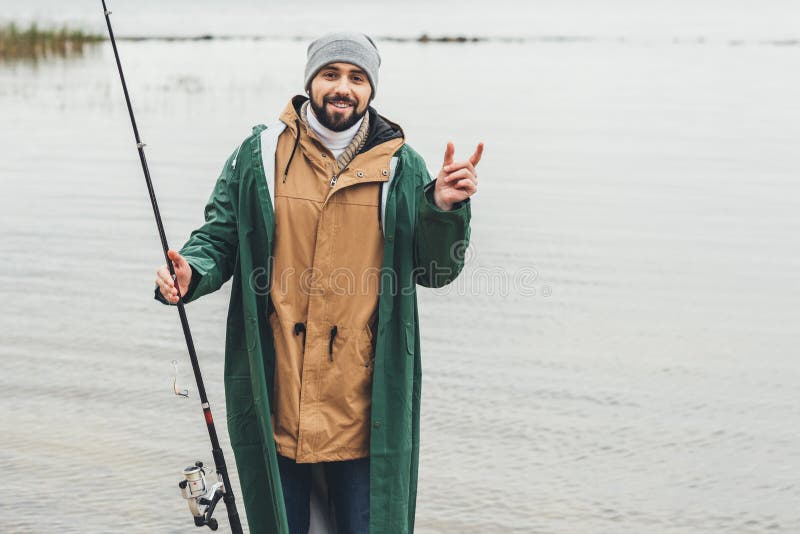 lächelnder Mann mit der Angelrute, die Größe von Fischen zeigt lizenzfreie stockbilder lächelnder Mann mit der Angelrute, die Größe von Fischen zeigt lizenzfreie stockbilder