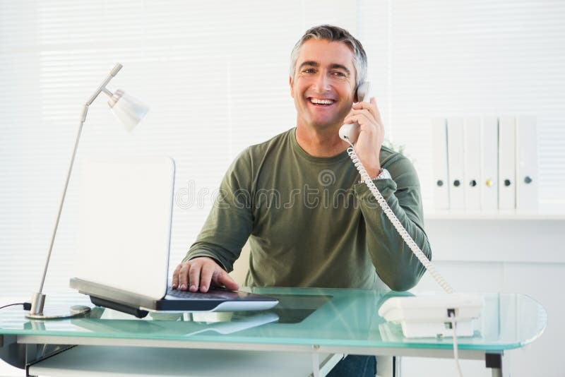 Lächelnder Mann am Telefon unter Verwendung des Laptops
