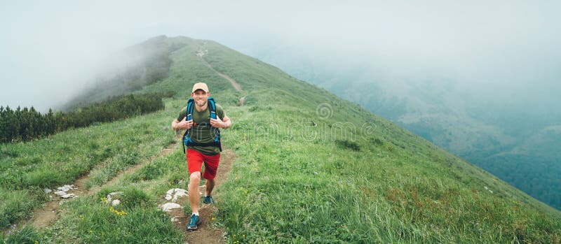 Lächelnder Wanderermann, der durch den nebeligen Gebirgszugweg des wolkigen Wetters mit Rucksack geht Aktives Sportwandern gesund stockfotos Lächelnder Wanderermann, der durch den nebeligen Gebirgszugweg des wolkigen Wetters mit Rucksack geht Aktives Sportwandern gesund stockfotos