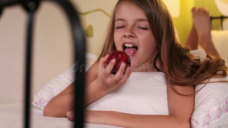 Lächelndes glückliches Mädchen, das einen Apfel im Bett isst