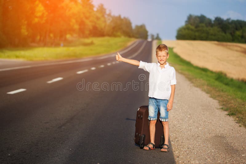 Lächelndes Kind mit dem reisenden Per Anhalter fahren des Koffers Sommerstraße lizenzfreie stockfotografie Lächelndes Kind mit dem reisenden Per Anhalter fahren des Koffers Sommerstraße lizenzfreie stockfotografie