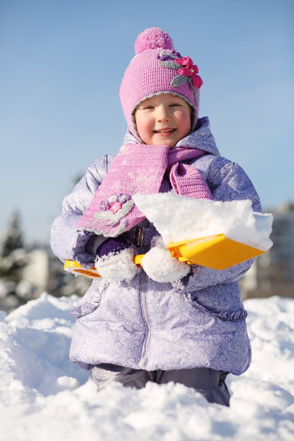 Lächelndes kleines Mädchen mit Schaufel zeigt Schnee in der Schneewehe lizenzfreie stockfotografie Lächelndes kleines Mädchen mit Schaufel zeigt Schnee in der Schneewehe lizenzfreie stockfotografie