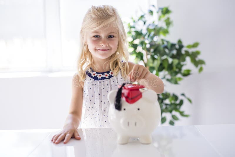 Lächelndes kleines Mädchen mit Sparschwein und Geld zu Hause