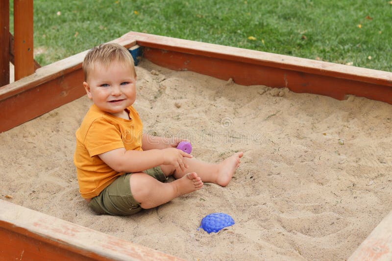 Lächelndes Kleinkind sitzend in einer hölzernen Sandbox Spielzeit mit bunten Spielzeug an einem sonnigen Tag stockfoto