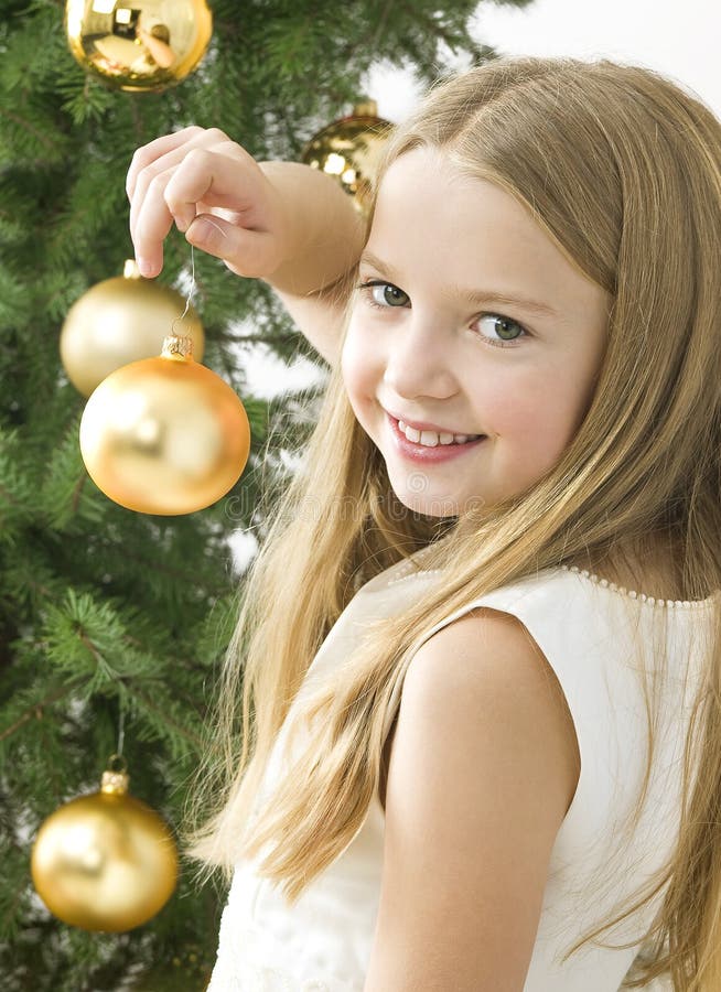 Lächelndes Mädchen mit Weihnachtskugeln nahe bei grünem tr