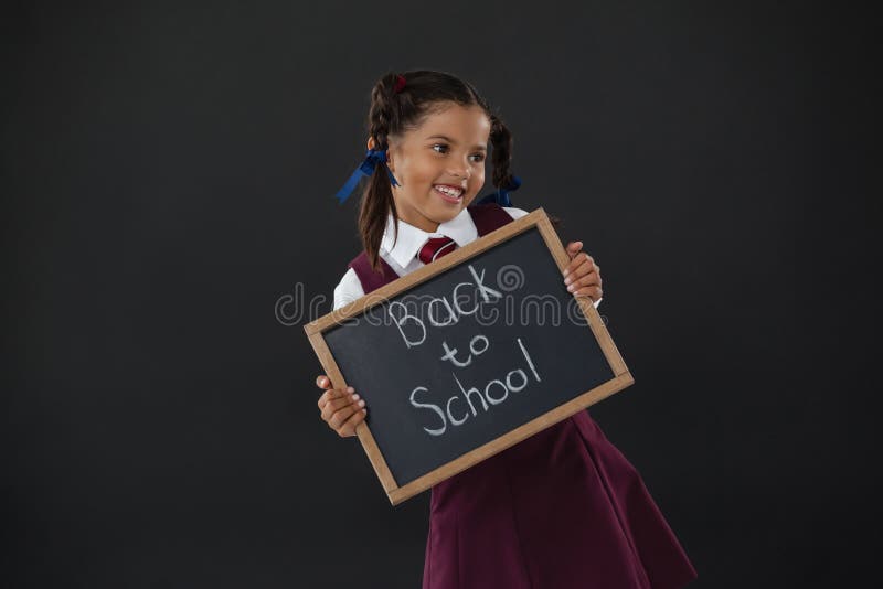 Lächelndes Schulmädchen, das Schiefer mit Text gegen Tafel hält