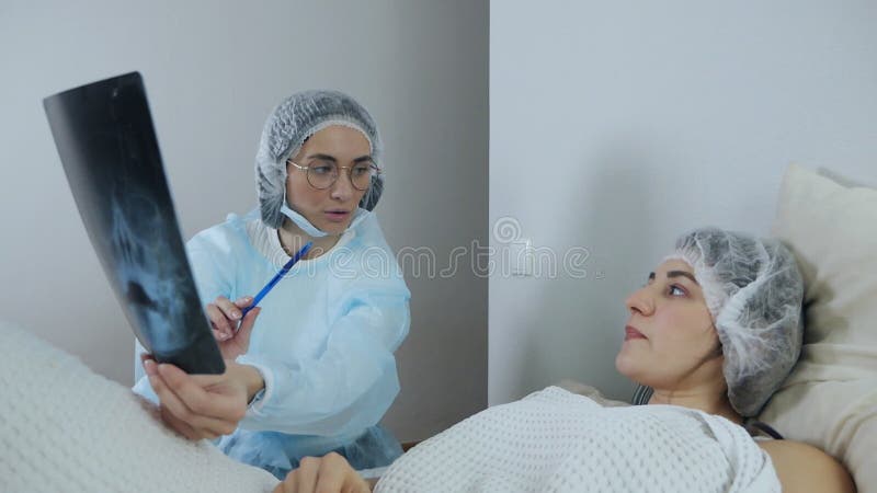 Läkare som tittar på och diskuterar resultaten av en datortomografi hos en patient som ligger på sängen i ett akutrum arkivfilmer