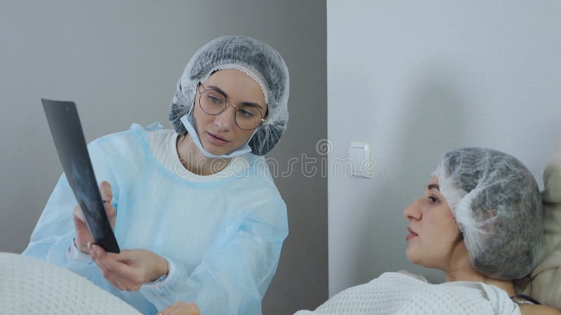 Läkare som tittar på och diskuterar resultaten av en datortomografi hos en patient som ligger på sängen i ett akutrum arkivfilmer