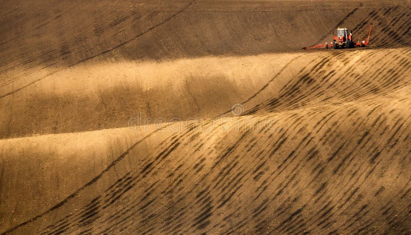 Agriculture Tractor Cultivating Brown Field And Creating Abstract Background Texture.Czech Republic. Europe Agricultural Landscape With Red Tractor Plowing A Striped Brown Field In South Moravia At Sunset, Beautiful View On Rolling Hills, Czech Republic. Agriculture Tractor Cultivating Brown Field And Creating Abstract Background Texture.Czech Republic. Europe Agricultural Landscape With Red Tractor Plowing A Striped Brown Field In South Moravia At Sunset, Beautiful View On Rolling Hills, Czech Republic.