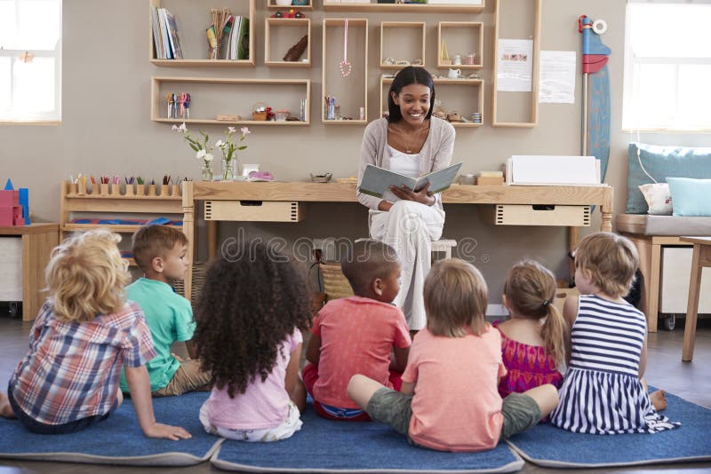 Teacher At Montessori School Reading To Children At Story Time. Teacher At Montessori School Reading To Children At Story Time