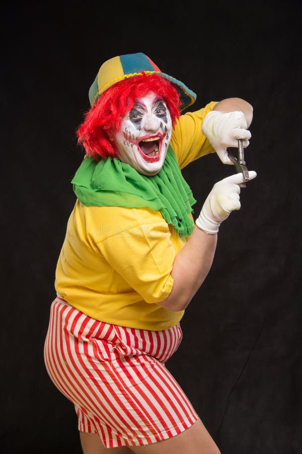 Läskig ond clown med ett fult leende och ett par av plattång på en bl royaltyfria foton Läskig ond clown med ett fult leende och ett par av plattång på en bl royaltyfria foton