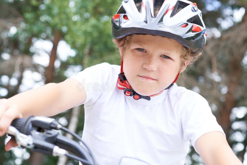 Lågvinkelsikt för en leende ung pojke i en hjälm som cyklar på sommarparken royaltyfria foton
