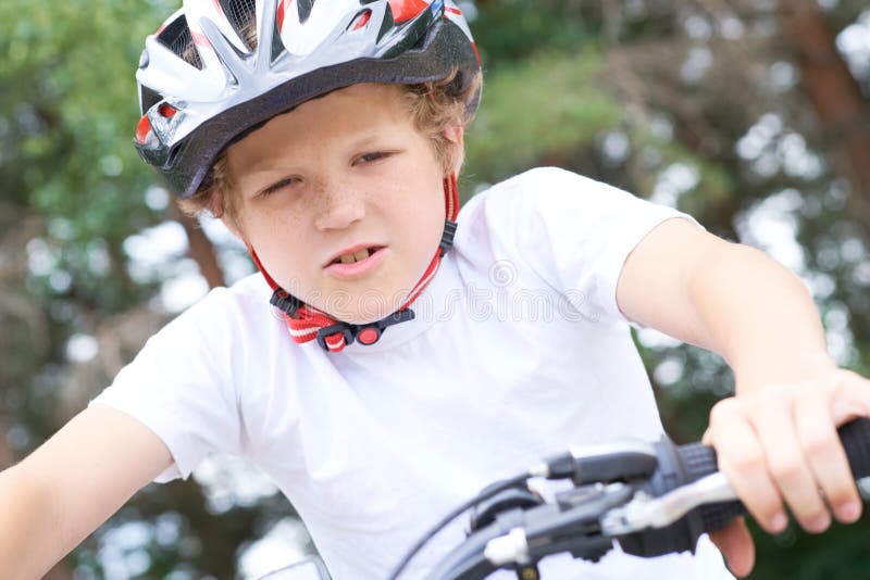 Lågvinkelsikt för en leende ung pojke i en hjälm som cyklar på sommarparken arkivbilder