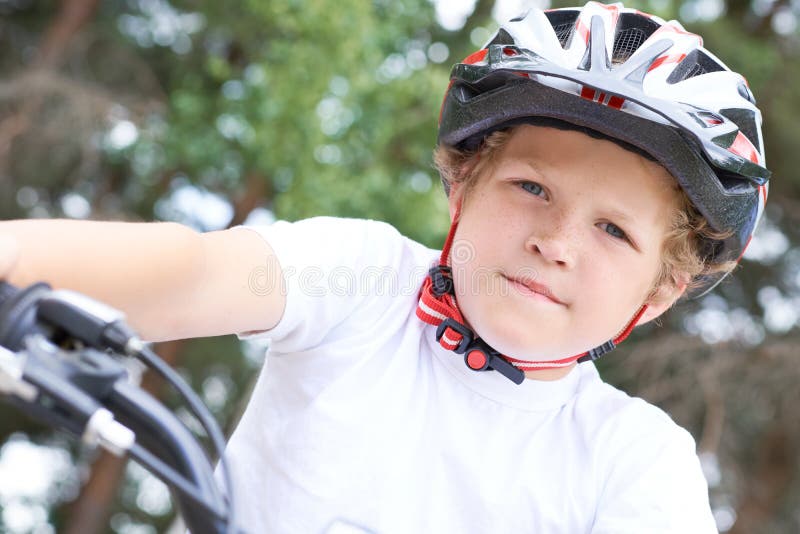 Lågvinkelsikt för en leende ung pojke i en hjälm som cyklar på sommarparken arkivbilder