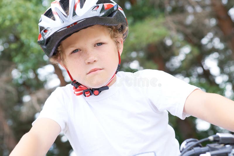 Lågvinkelsikt för en leende ung pojke i en hjälm som cyklar på sommarparken royaltyfri bild