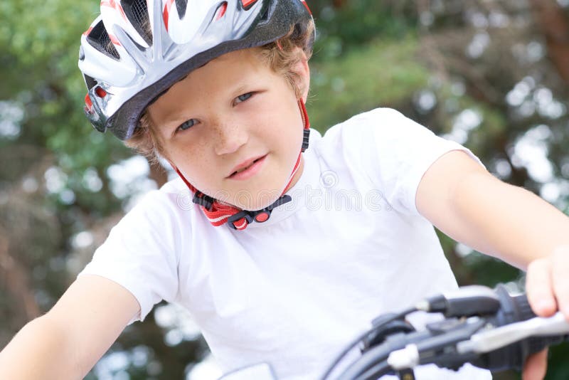 Lågvinkelsikt för en leende ung pojke i en hjälm som cyklar på sommarparken royaltyfri foto