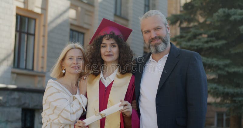 Långsam rörelse av lyckliga familjerföräldrar och dotter som står på campus på universitetsdag och tittar på kamera som leker