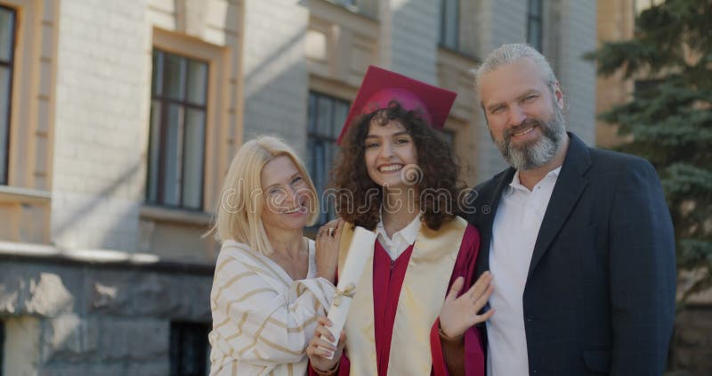 Långsam rörelse av unga kvinnor med akademisk examen och föräldrar som är stolta över sin mamma och pappa på campus