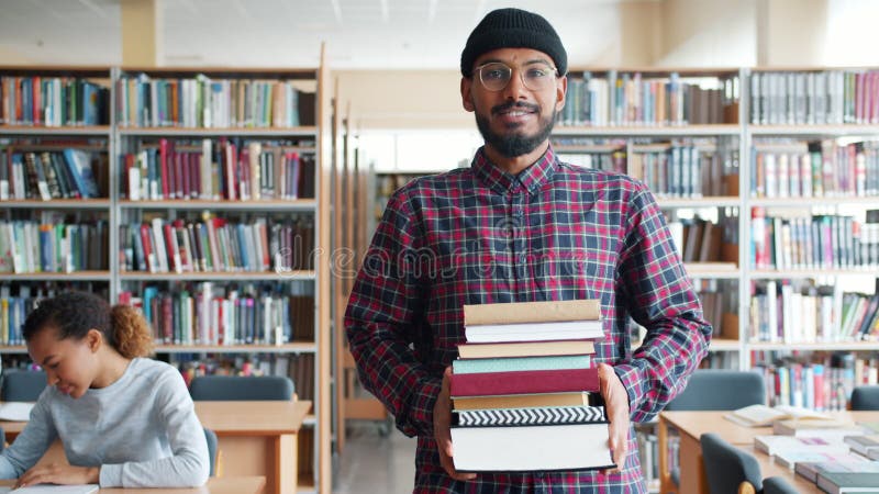 Långsam rörelse för en stilig afrikansk student som går i biblioteket med böcker stock video