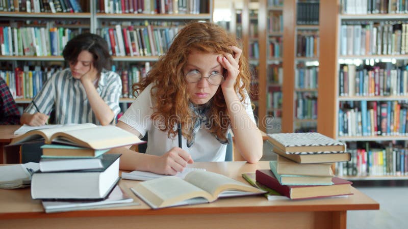 Långsam rörelse för en sömnig dam som arbetar i biblioteket och sedan sover huvudet på skrivbordet stock video