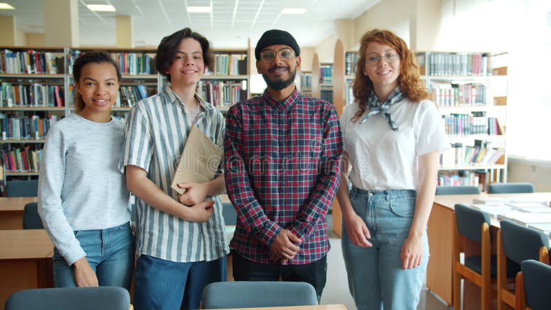 Långsam rörelse för glada studenter som står i bibliotek med böcker arkivfilmer