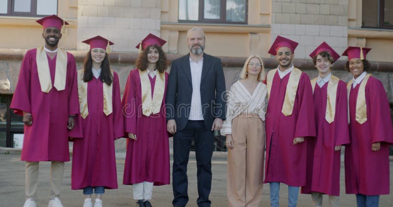 Långsam rörelse för studenter i graderingsmantel och hatt och mogna professorer som står på campus leende