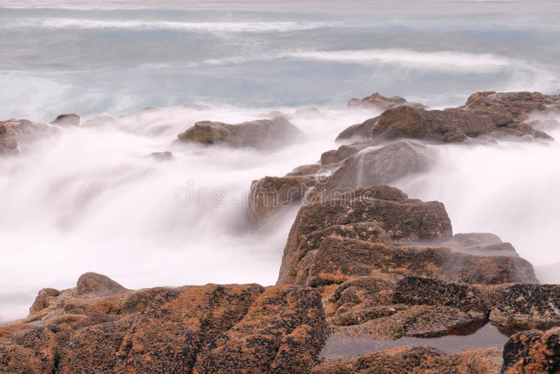 LÅNGT EXPONERINGSFOTOGRAFI AV EN KLIPPA SOM PEPPRAS AV VÅGORNA AV HAVET fotografering för bildbyråer LÅNGT EXPONERINGSFOTOGRAFI AV EN KLIPPA SOM PEPPRAS AV VÅGORNA AV HAVET fotografering för bildbyråer