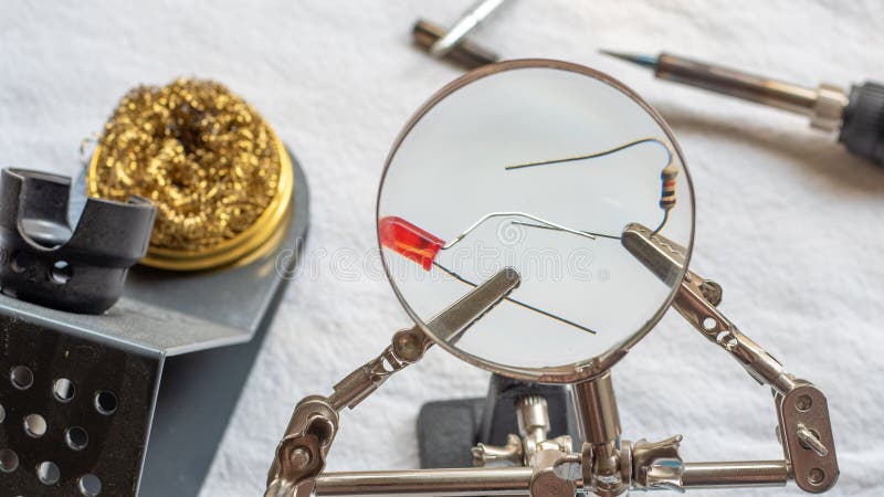 Löda ett motstånd och LETT med ett förstoringsglas, med alligatorgem som rymmer delarna arkivbild Löda ett motstånd och LETT med ett förstoringsglas, med alligatorgem som rymmer delarna arkivbild
