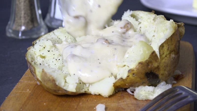 Löffeln der Landsoße mit Würstchen auf eine gebackene Kartoffel