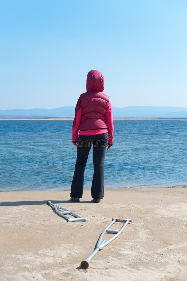 Woman stands at shore having left her crutches, back view. Woman stands at shore having left her crutches, back view