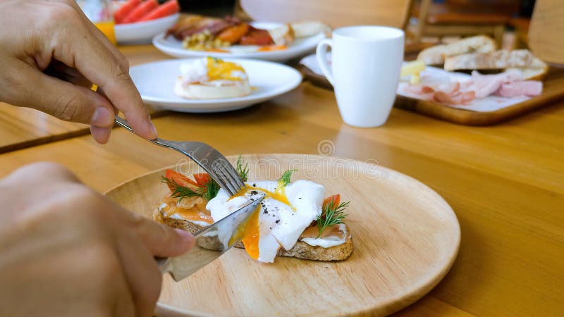 Mãos com faca e garfo cortando muffin inglês com ovos escalfados